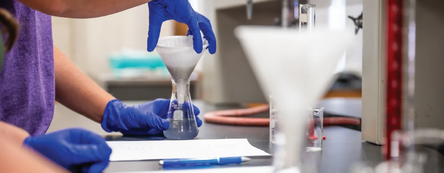 Gloved hands conducting chemistry experiment.